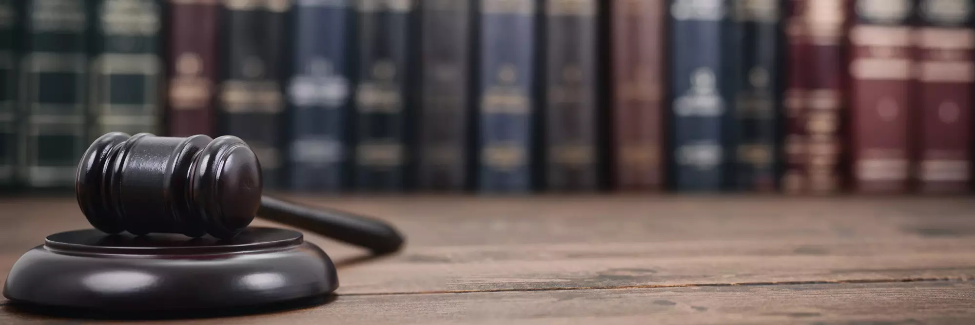 Diritto Civile. Martelletto di legno posato su un tavolo di legno, sullo sfondo si intravedono volumi di diritto in rilegatura.