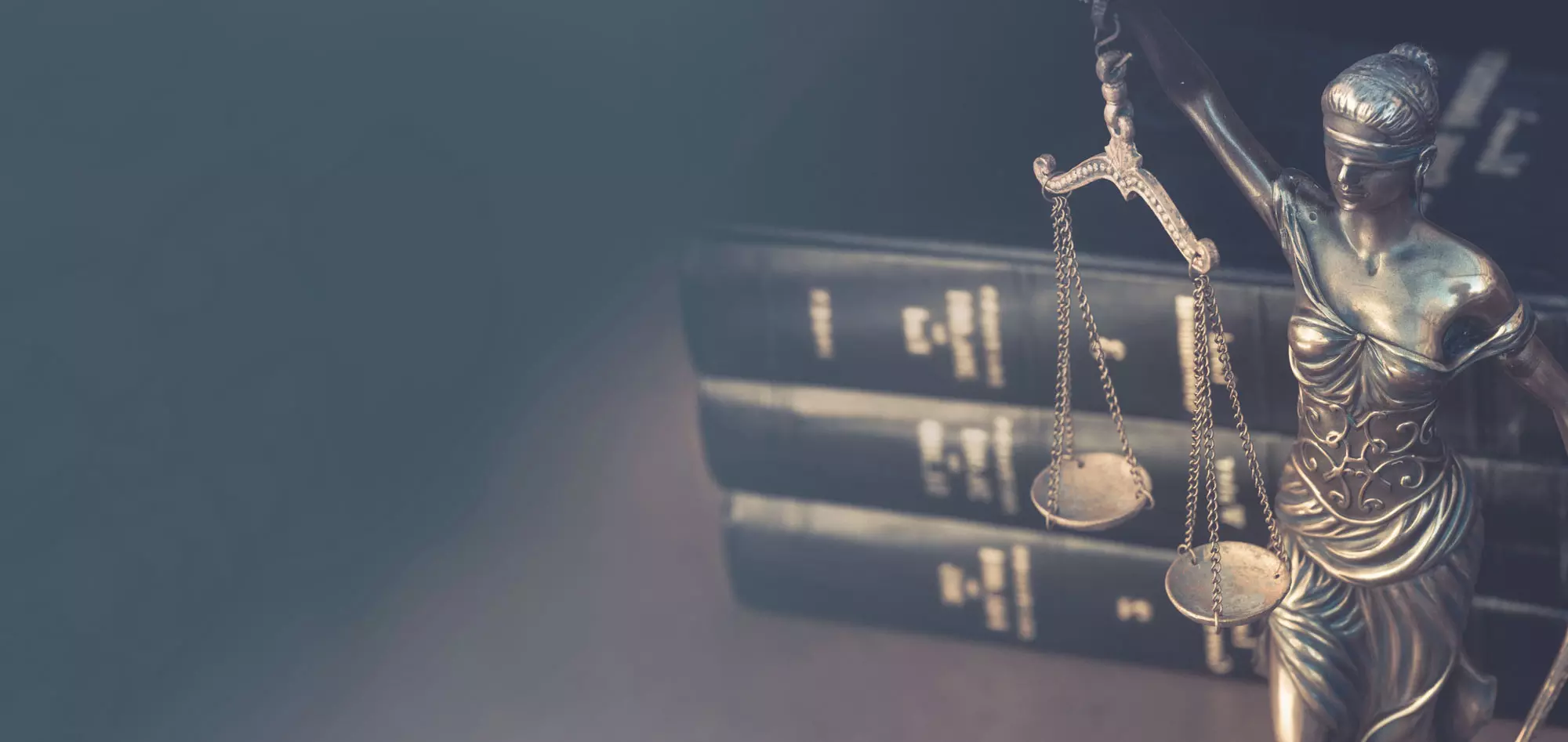 Una bilancia della giustizia in primo piano, con tre volumi di libri legali sullo sfondo, simbolo di diritto e giustizia.